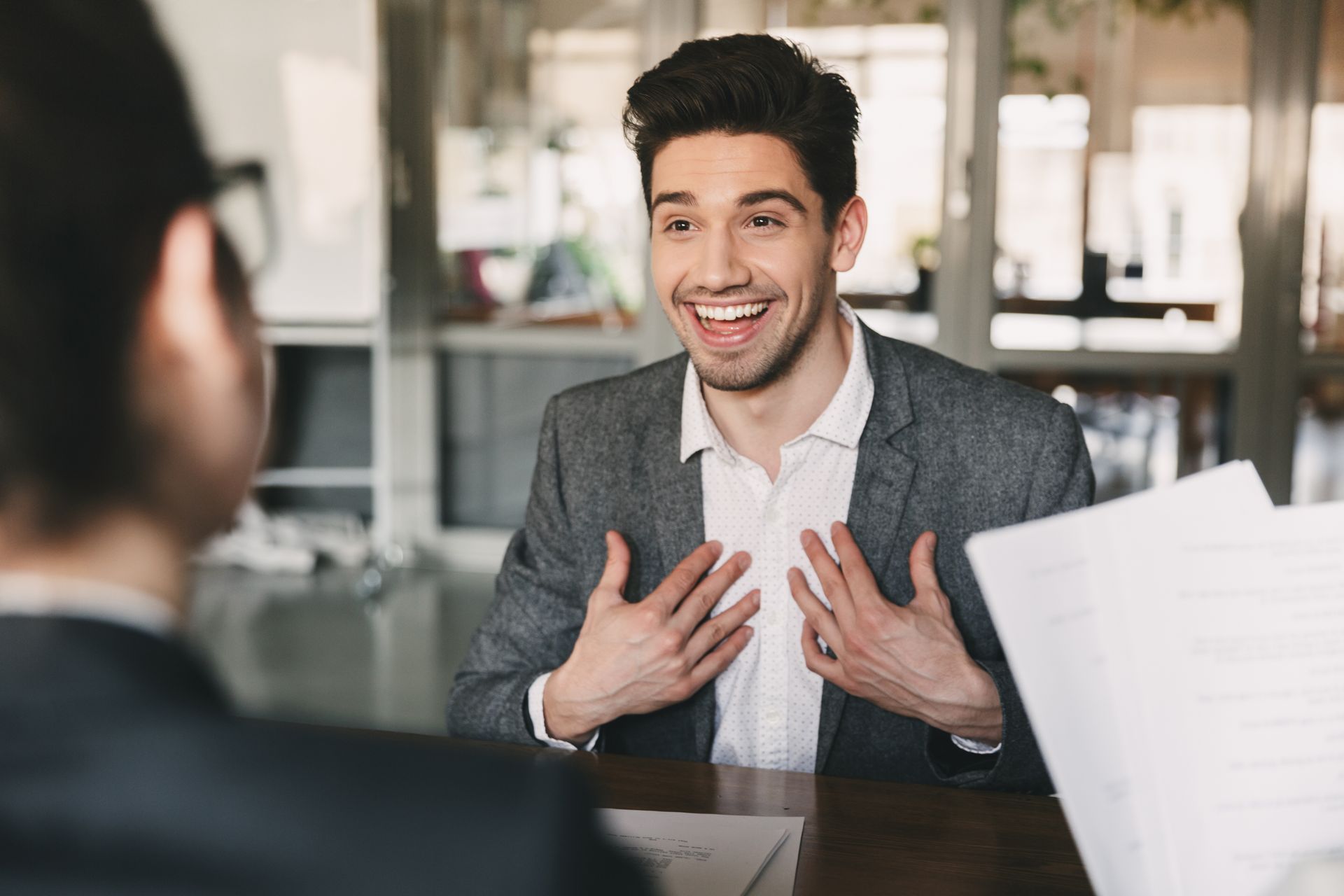 A man is sitting at a table talking to another man.
