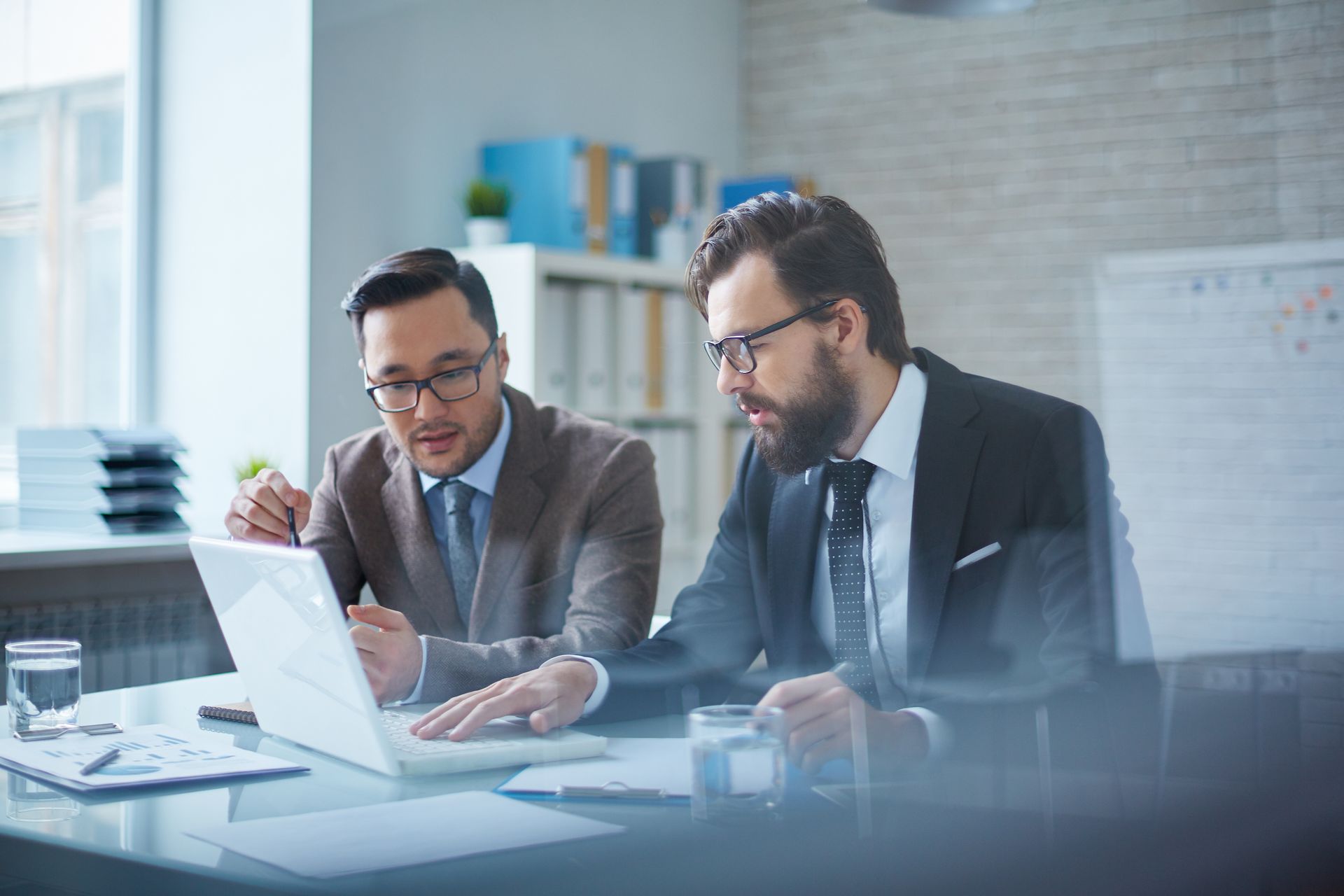 Two men are sitting at a table looking at a laptop computer.
