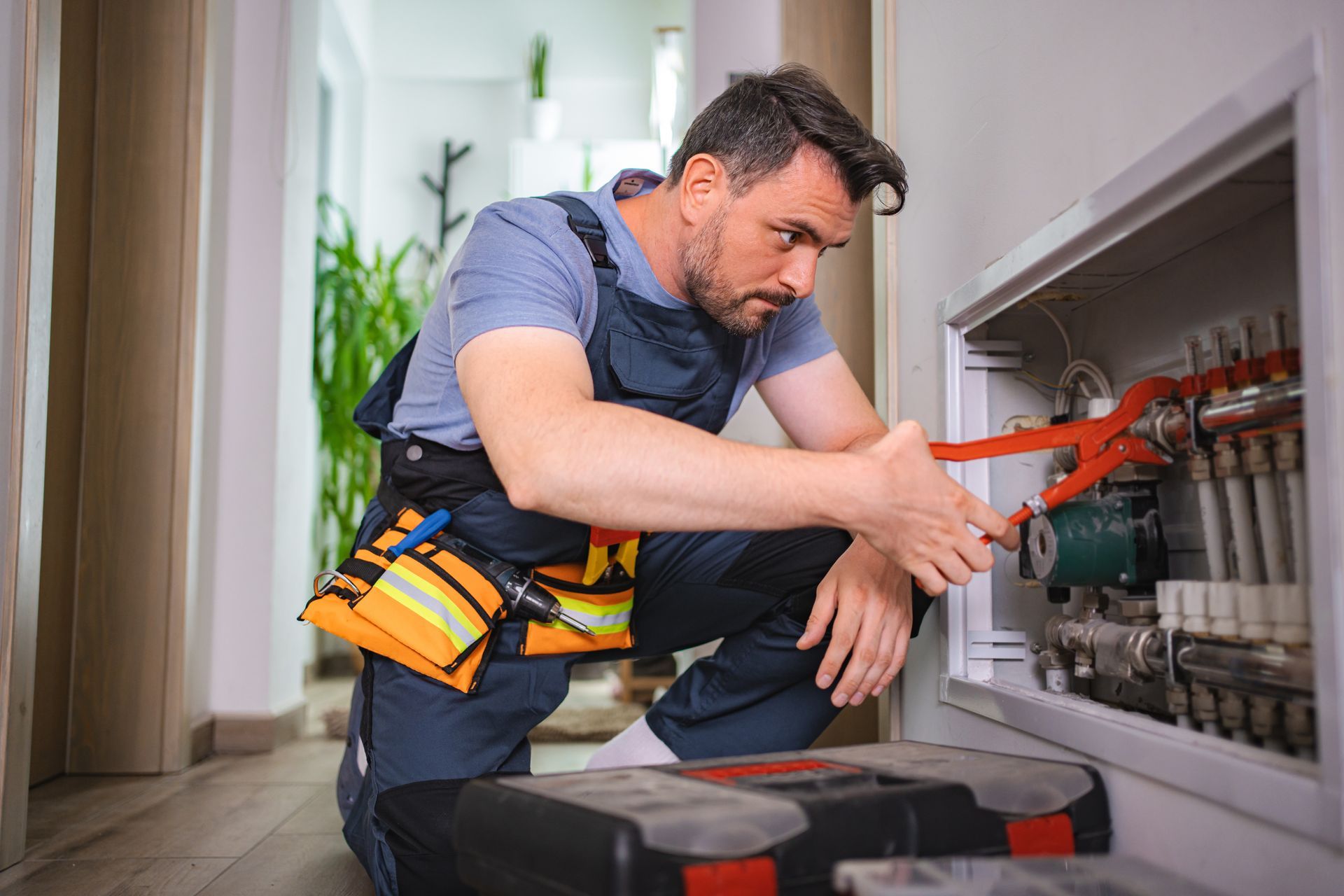 Technician adjusting plumbing valves with tools inside a residential utility cabinet.