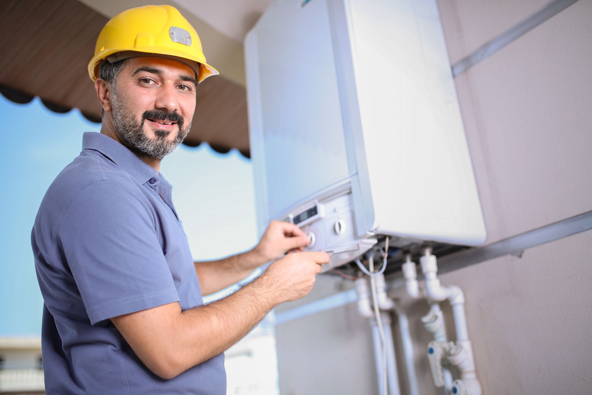 Worker adjusting controls on an outdoor boiler unit connected to exposed plumbing lines.