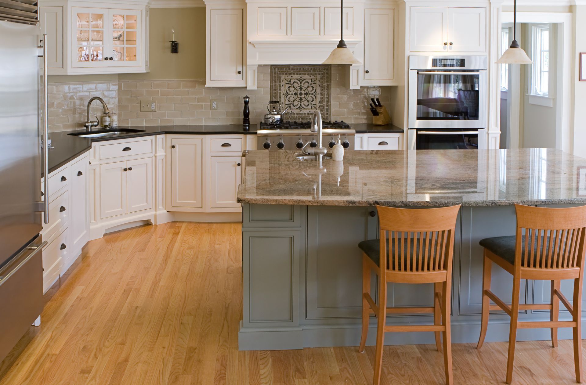 Kitchen with white cabinets, wood floors, and a gray island with granite countertops.