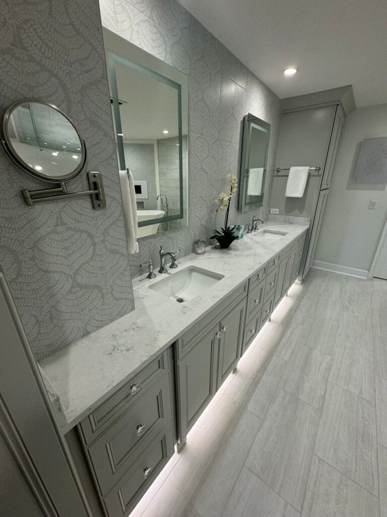 Bathroom with light gray cabinets, white countertop, silver fixtures, and patterned wallpaper.