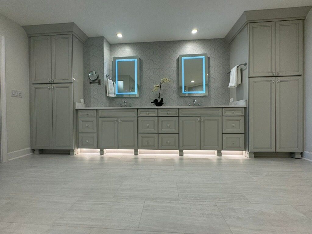 Modern gray bathroom with dual sinks, mirrors with blue lights, and tall storage cabinets.
