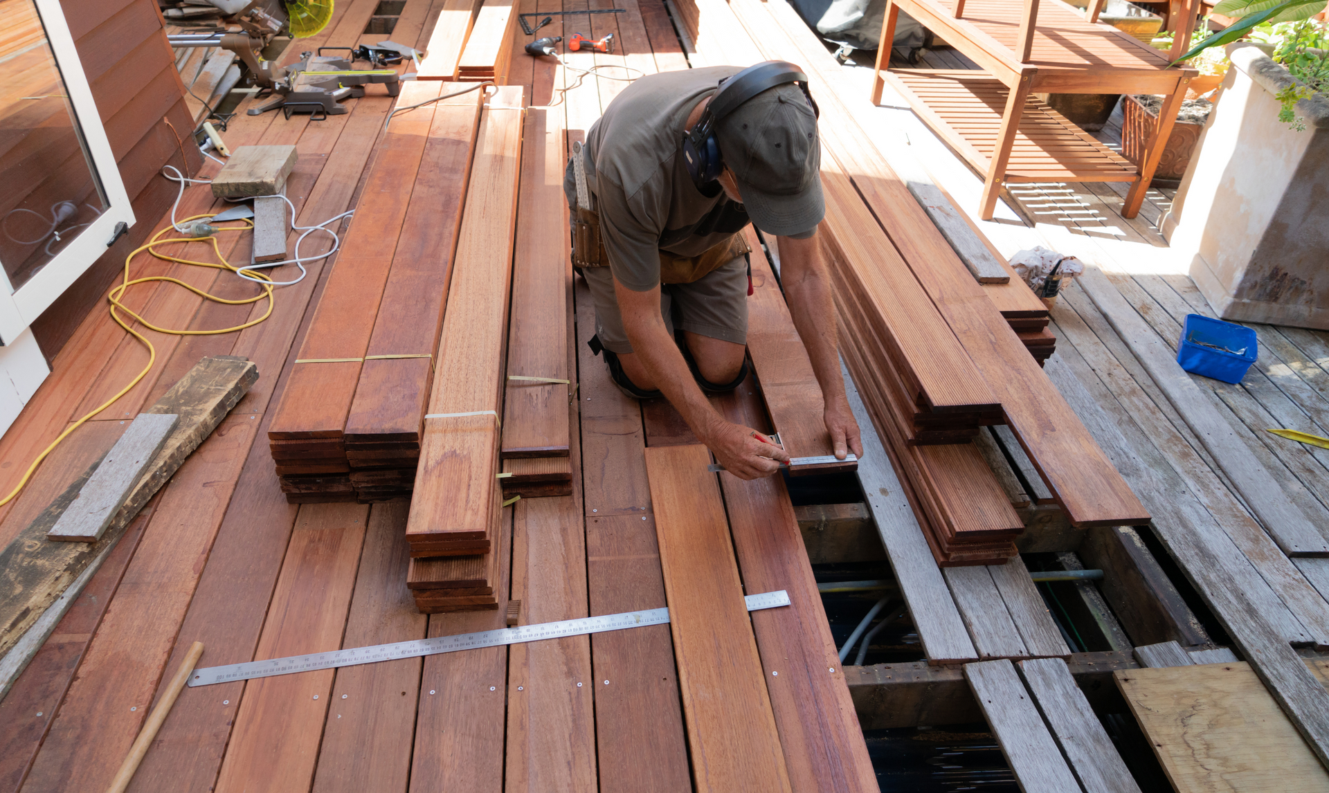 Man kneeling, measuring wood planks on a deck, preparing for construction.