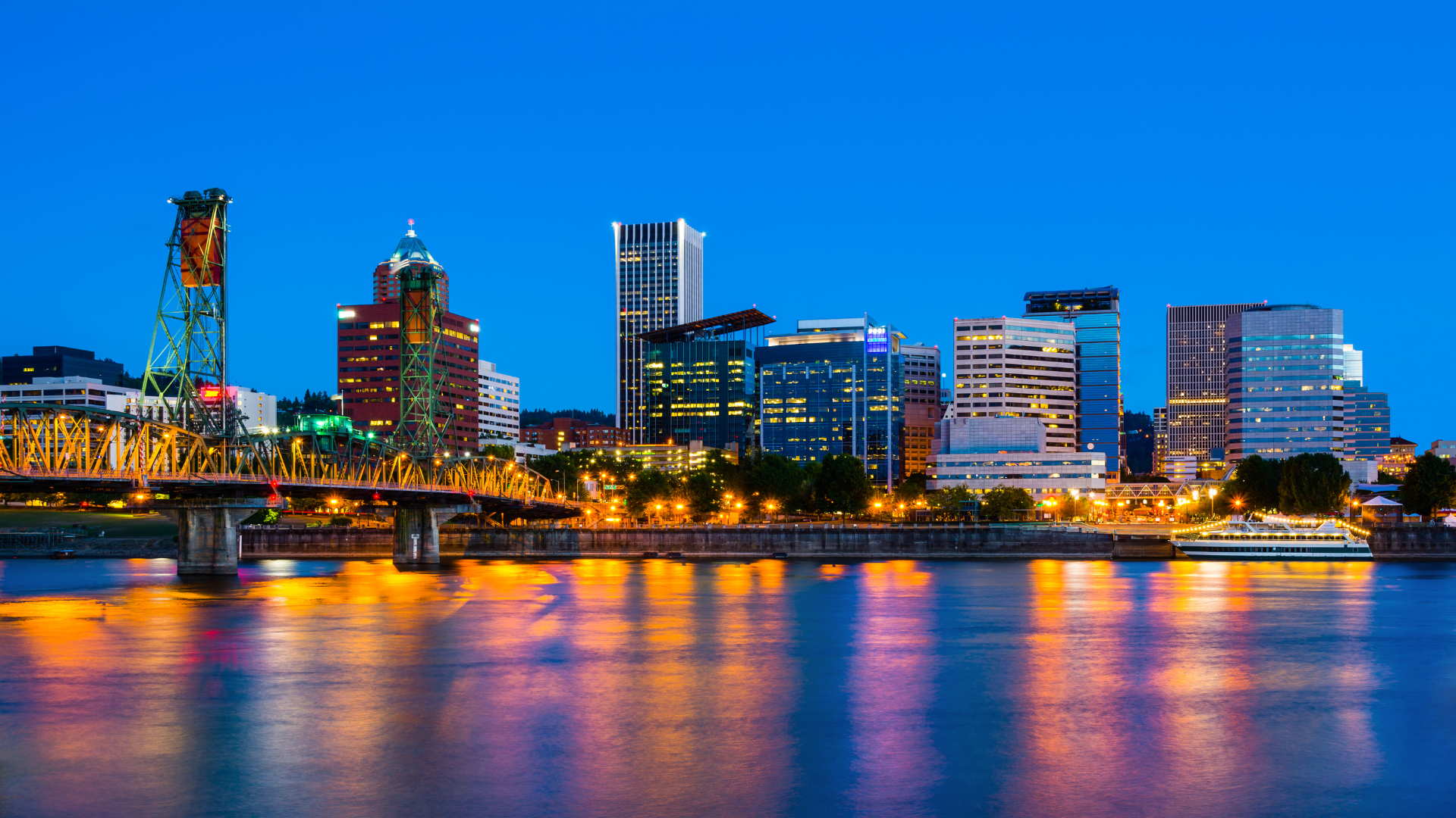 Portland, Oregon skyline at dusk reflected in the Willamette River, buildings lit with golden lights.