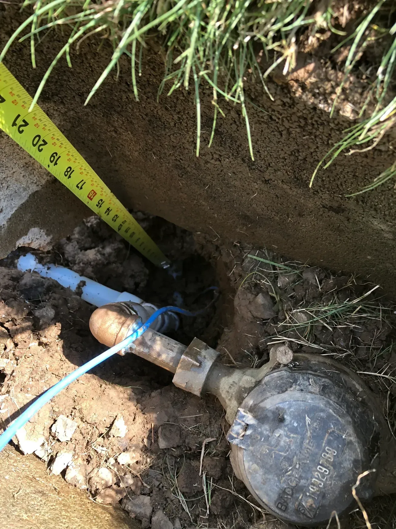 A water meter is sitting in the dirt next to a tape measure.