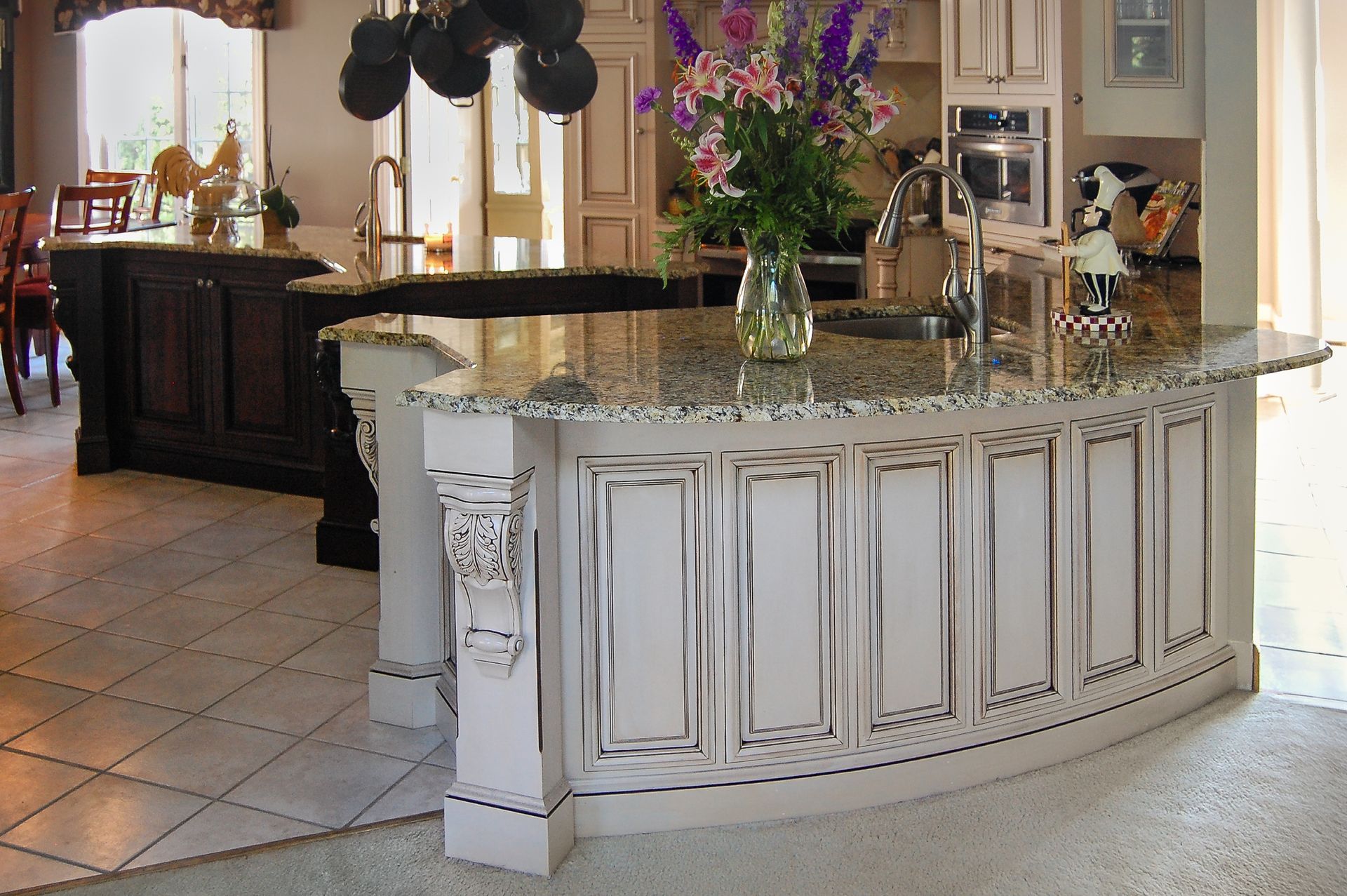 A modern kitchen with grey cabinets, stainless steel appliances, and a large island with bar stools. Wooden floors provide contrast.