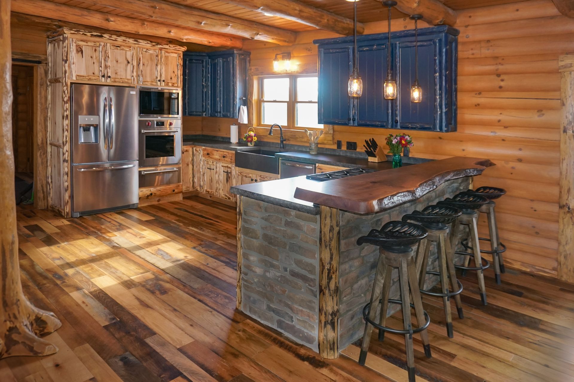 Custom rustic hand peeled wood kitchen cabinets with live edge island top wrapped in natural stone.