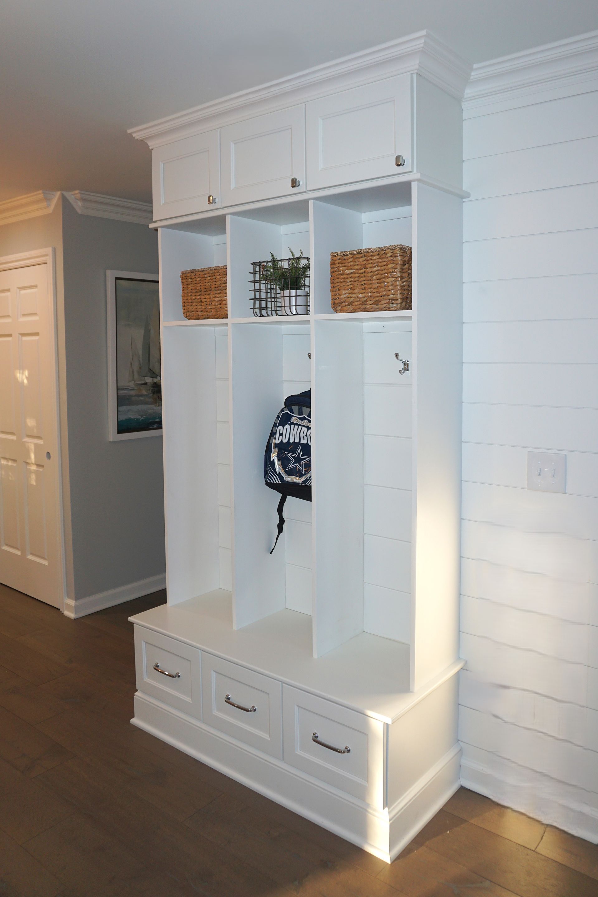 Custom white painted wood mudroom storage solution with coat hooks and seating.