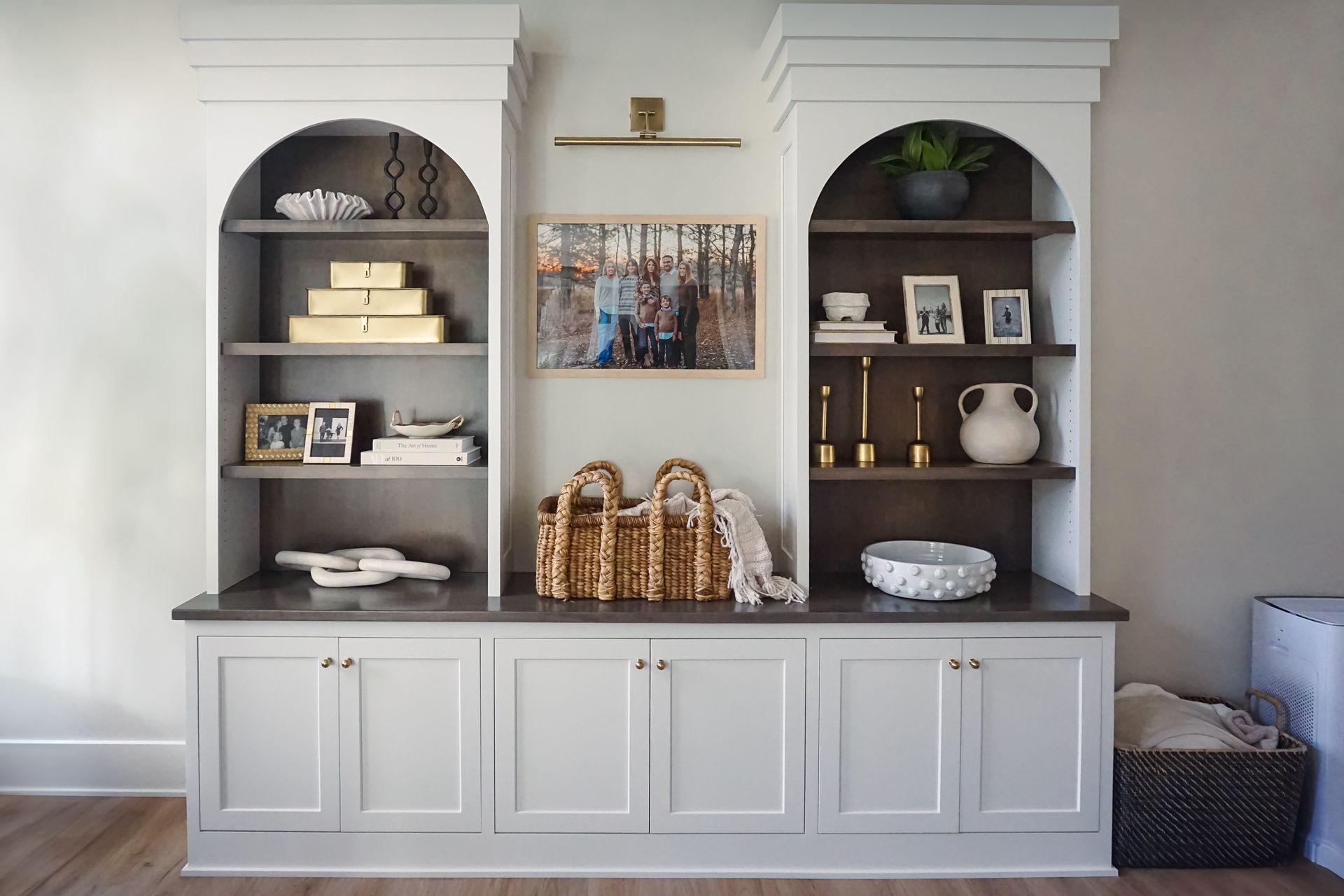 A long, white kitchen with marble countertops, stainless steel appliances, and dark wood floors.  Gold hardware accents the cabinetry.