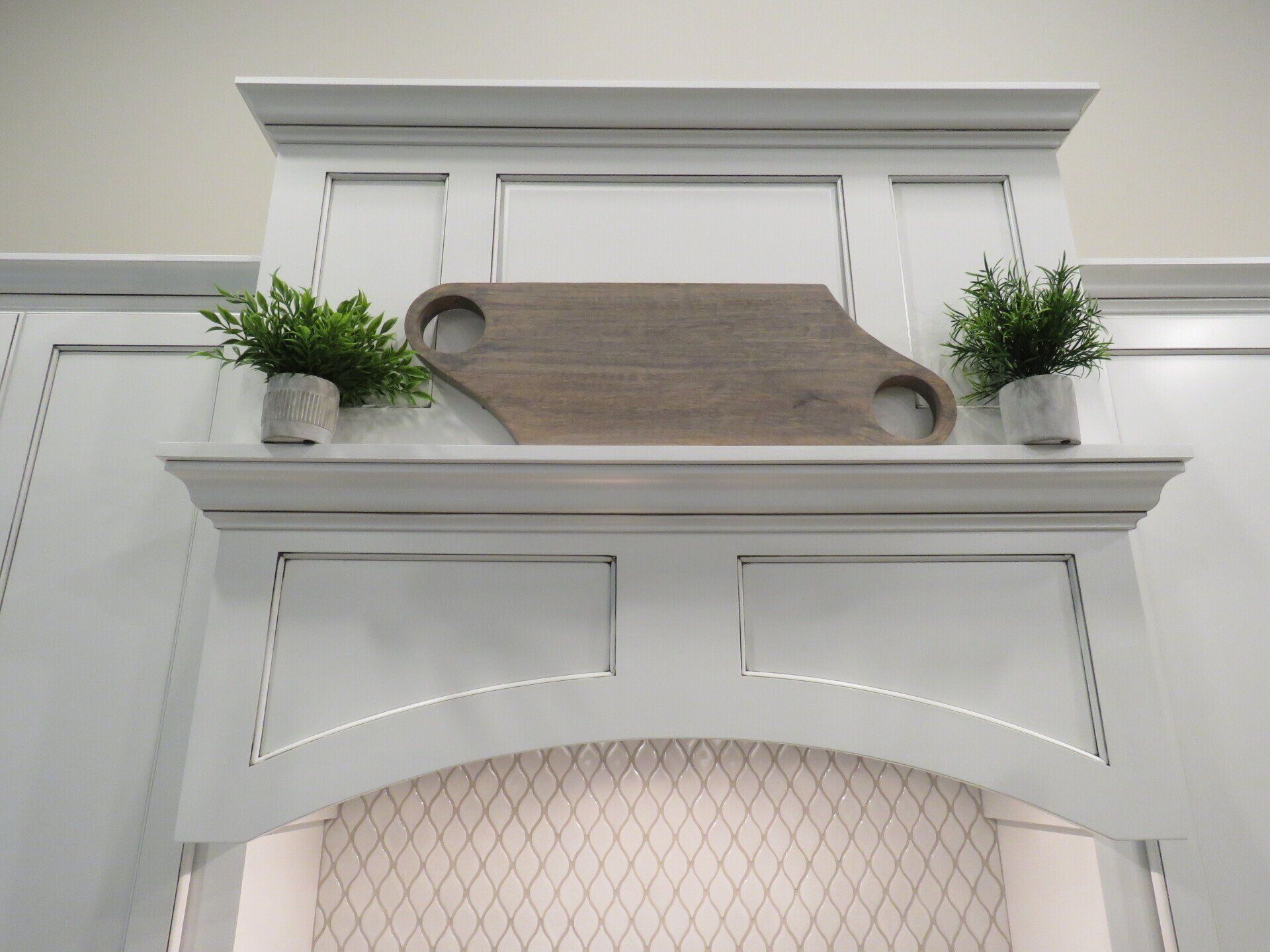 Custom white painted wood range hood with arched opening and panels.