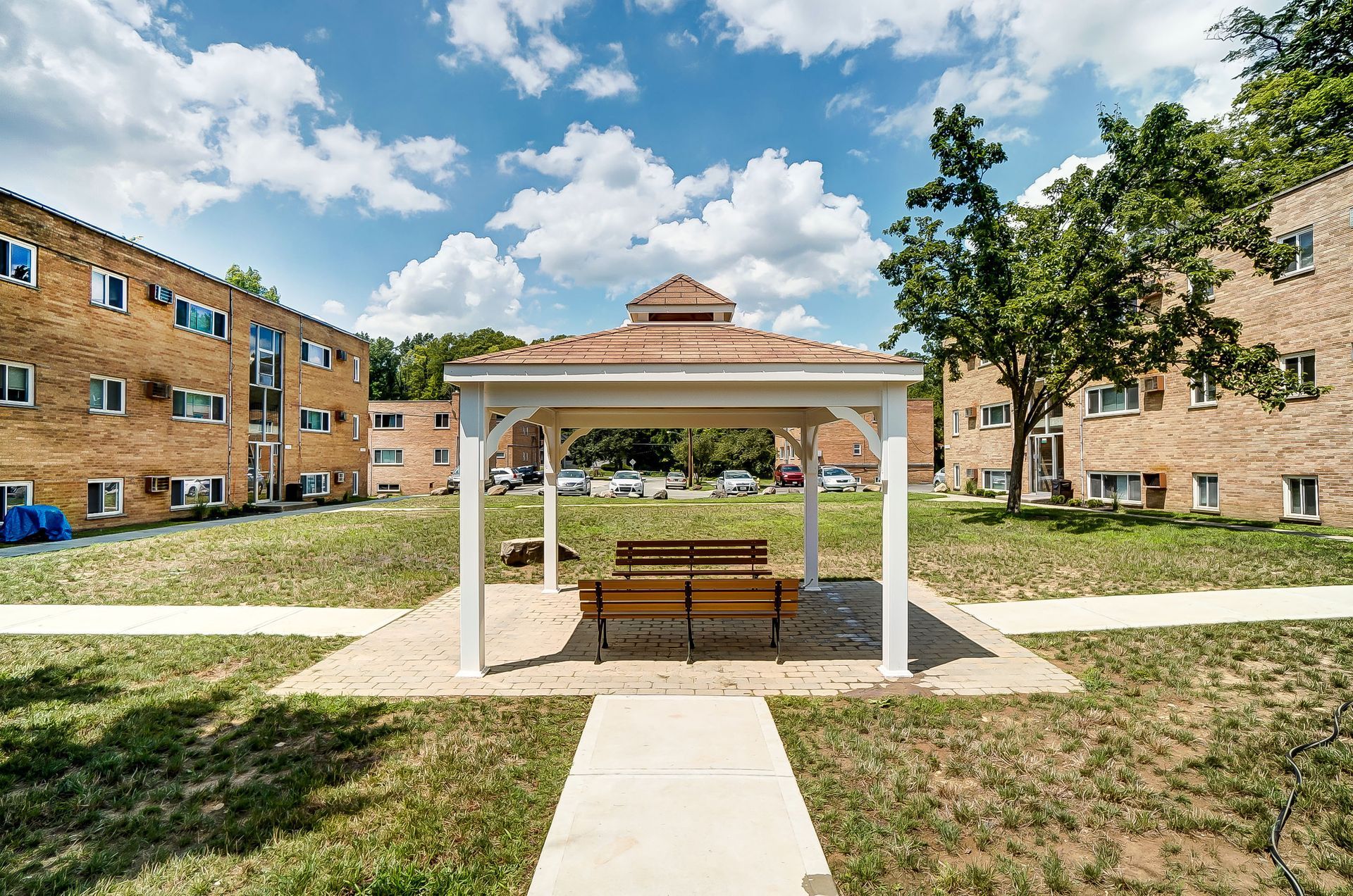A gazebo with a bench underneath it in front of a brick building.