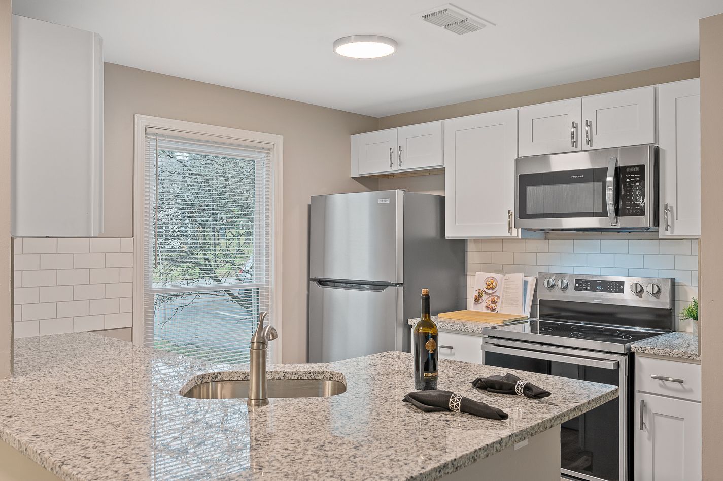 A kitchen with granite counter tops , stainless steel appliances , a refrigerator , stove and microwave.