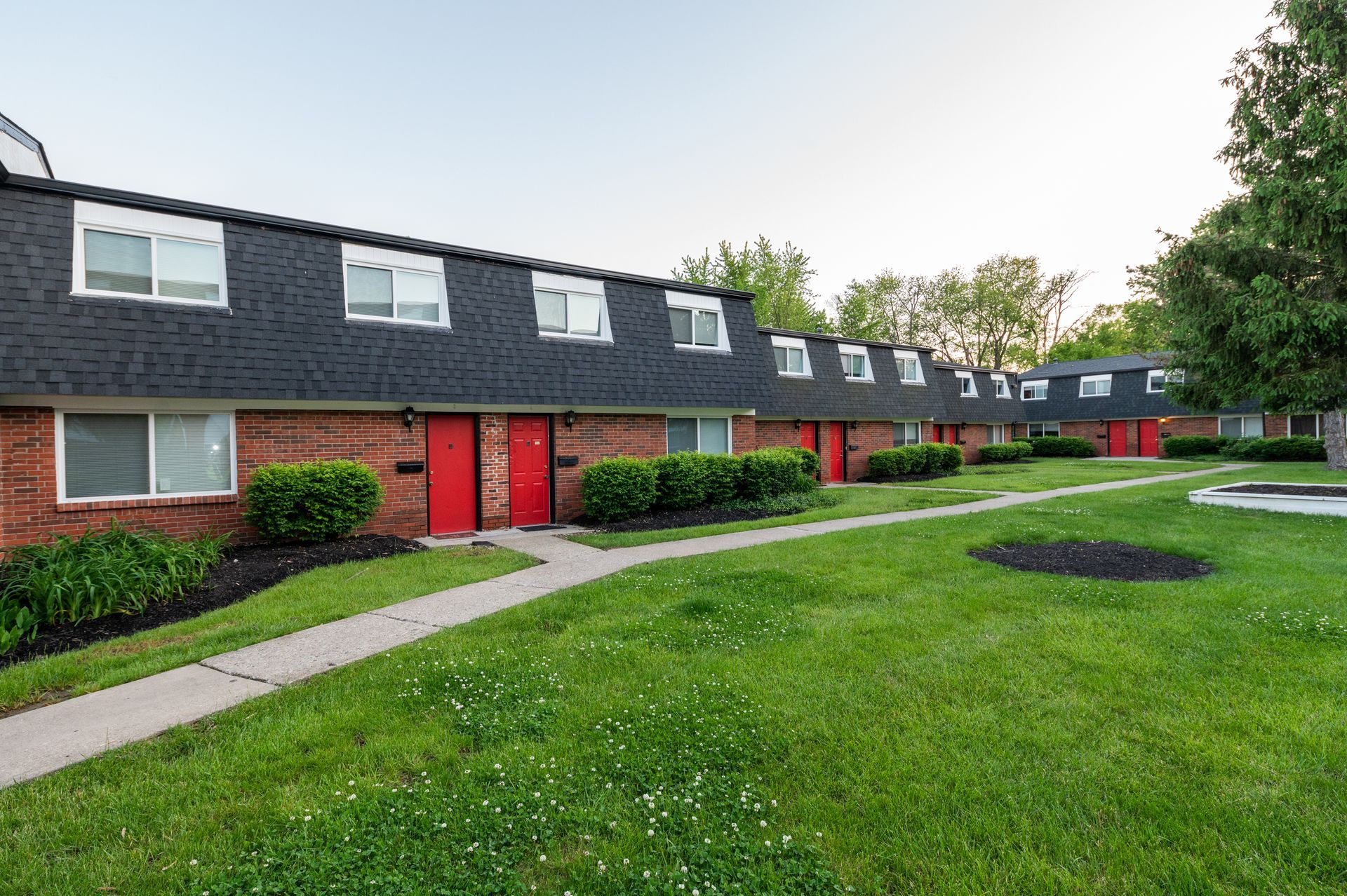 A row of apartment buildings with a lush green lawn in front of them.