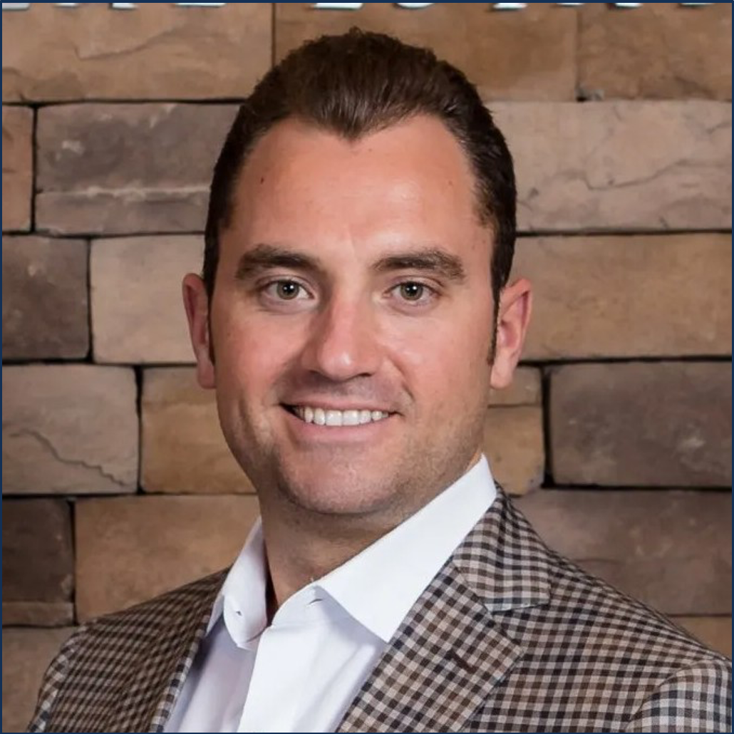 A man in a suit is standing in front of a brick wall.