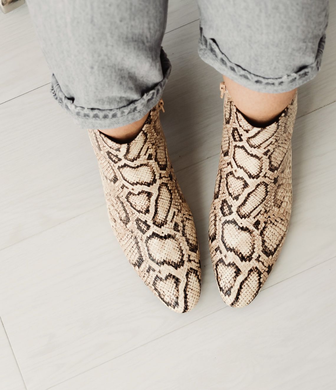 Person wearing snakeskin print ankle boots, cuffed jeans, indoor setting.