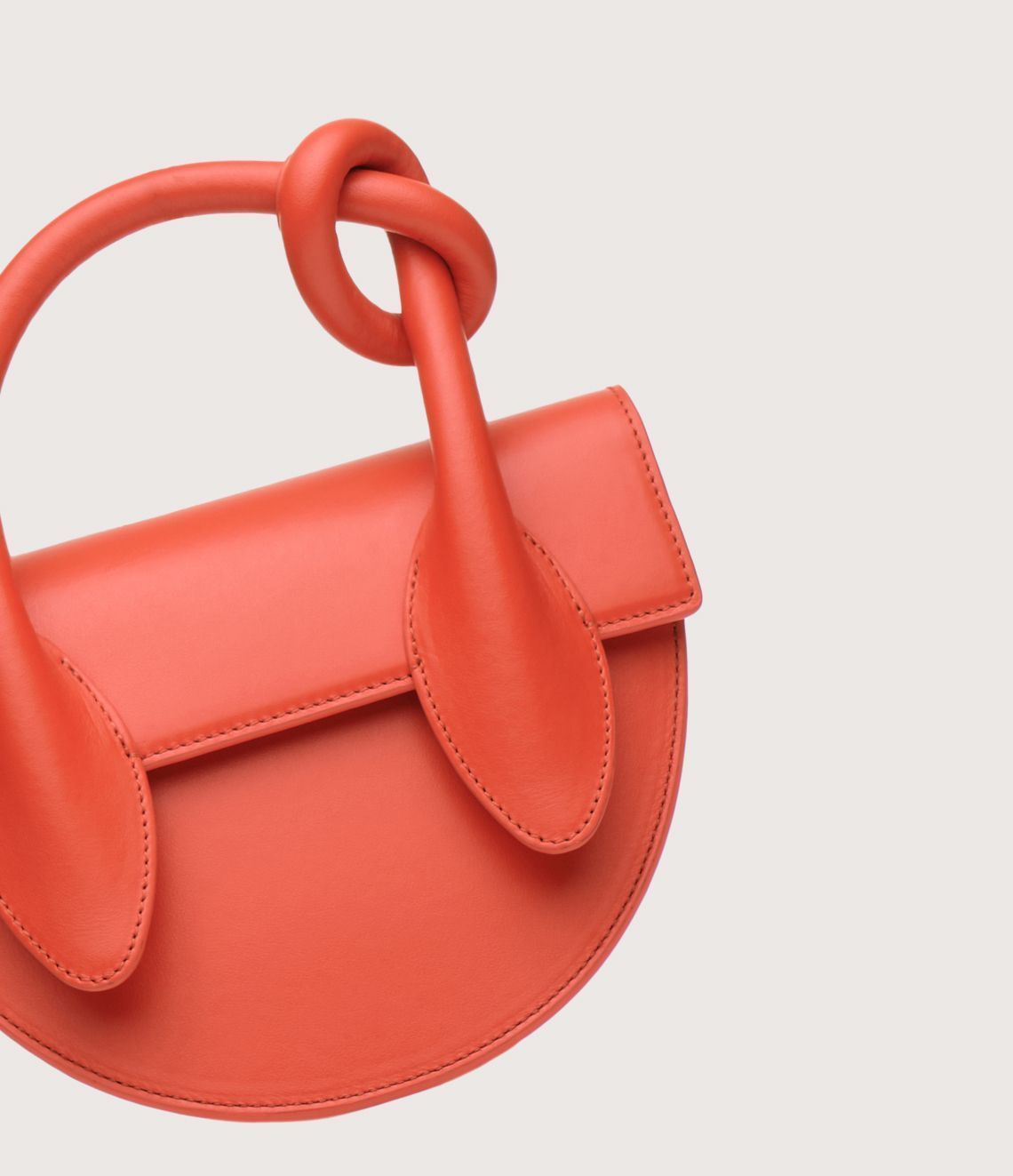 Orange, semi-circular handbag with a knotted handle and flap closure.