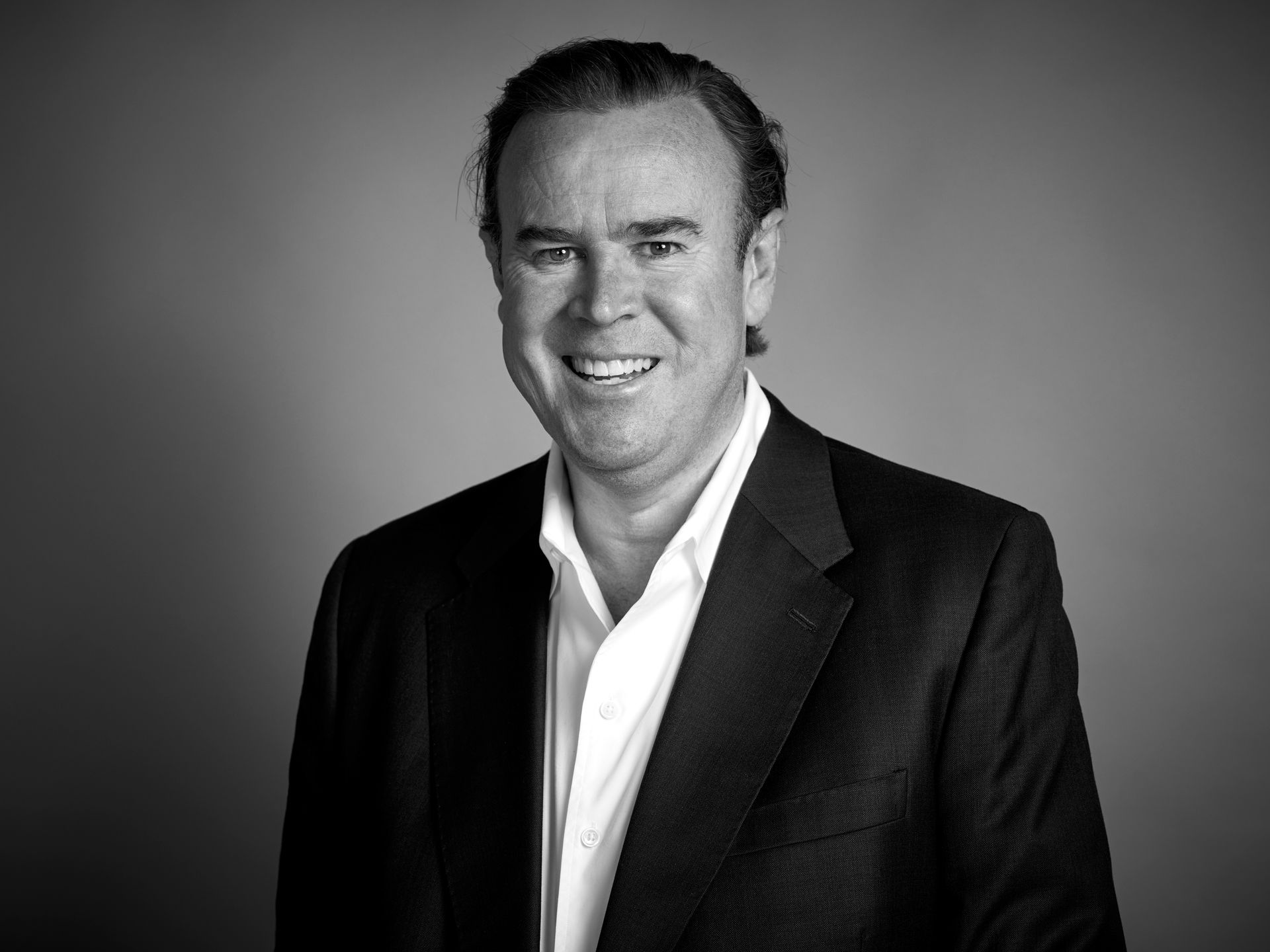 Man in a suit smiles, looking at the camera.