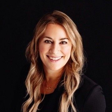 A woman with long blonde hair is smiling and wearing a black shirt.