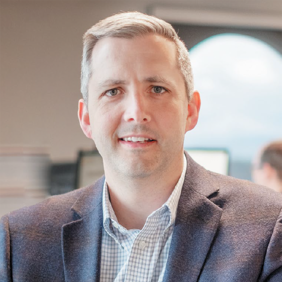 A man in a suit and plaid shirt is smiling for the camera.