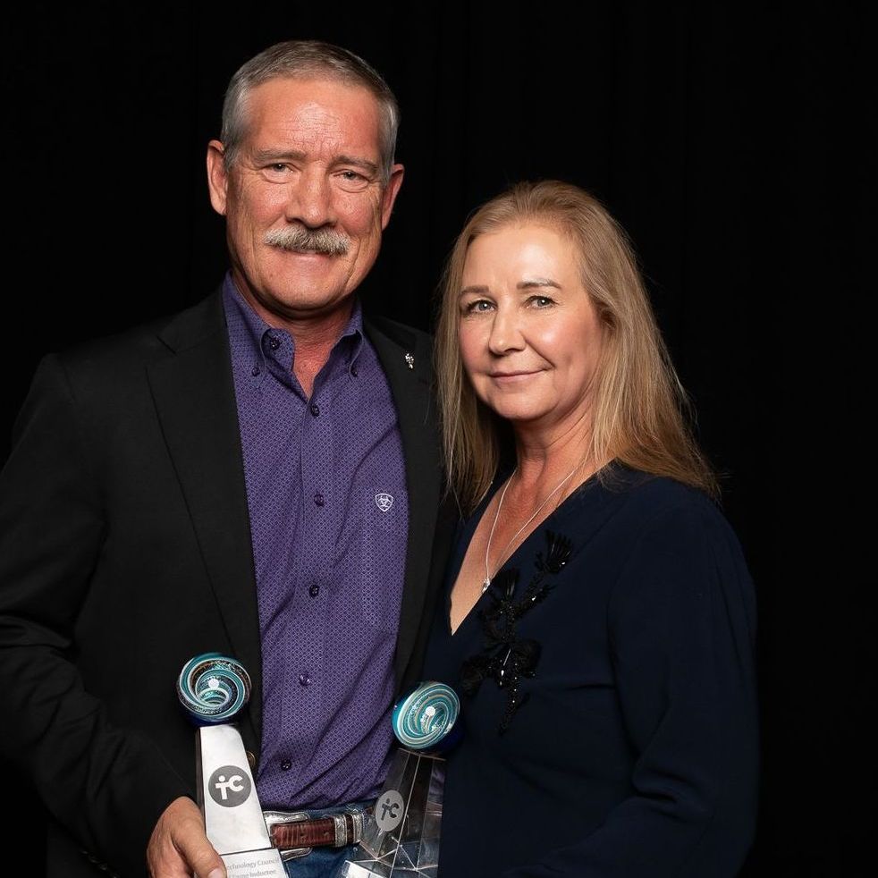 A man and a woman are standing next to each other holding trophies.