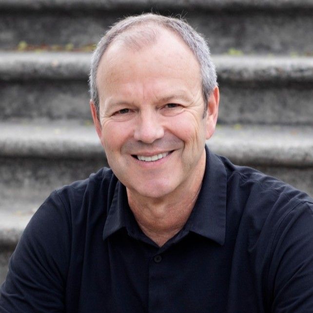 A man in a black shirt is smiling in front of some stairs