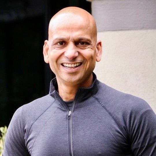 A bald man wearing a grey shirt is smiling for the camera