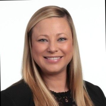 A woman with long blonde hair is smiling and wearing a black jacket.