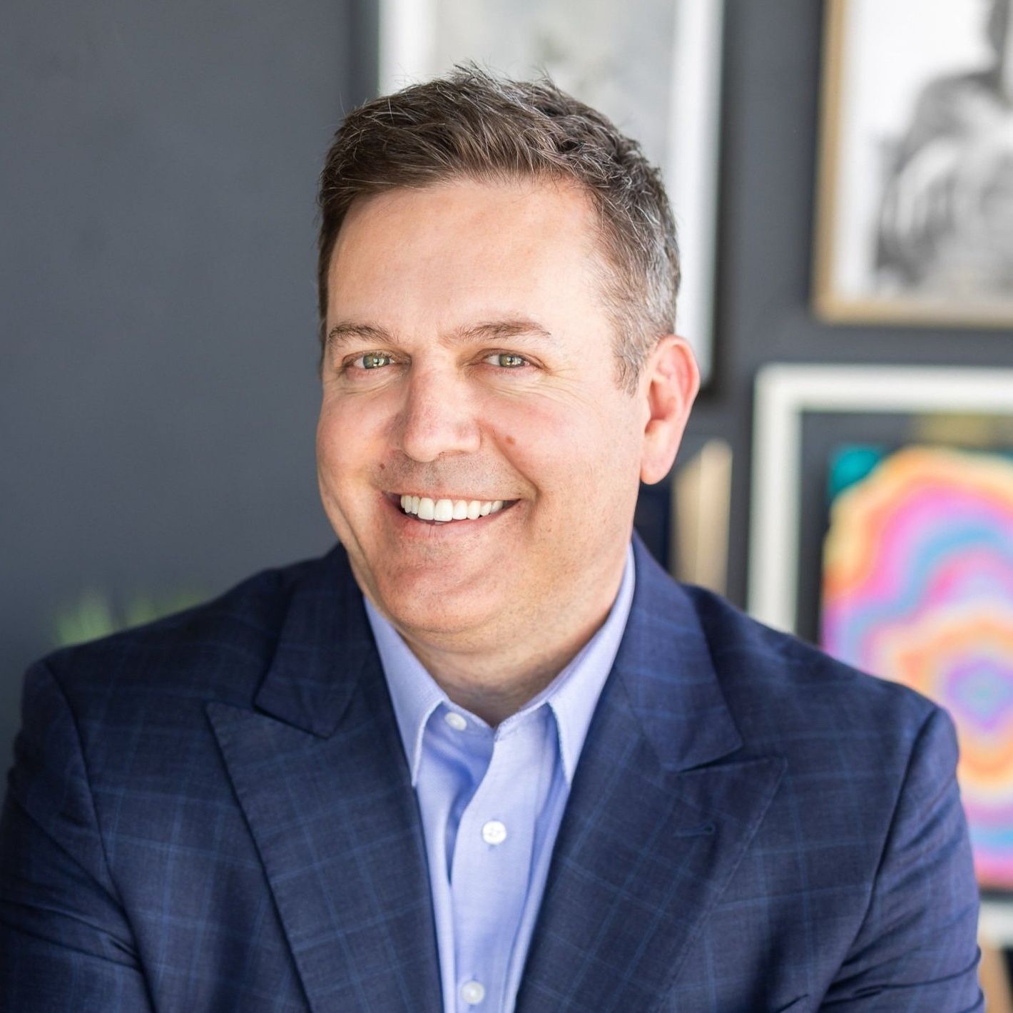 A man in a purple shirt is smiling with his arms crossed.