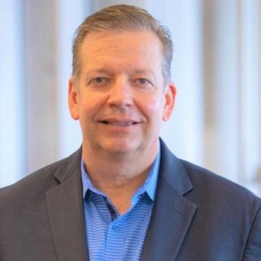 A man in a suit and blue shirt is smiling for the camera.