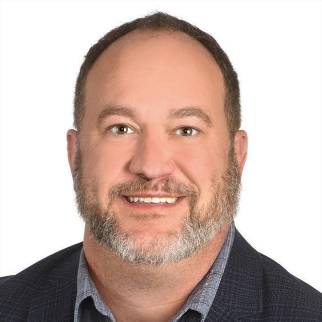 A man with a beard and a suit is smiling for the camera