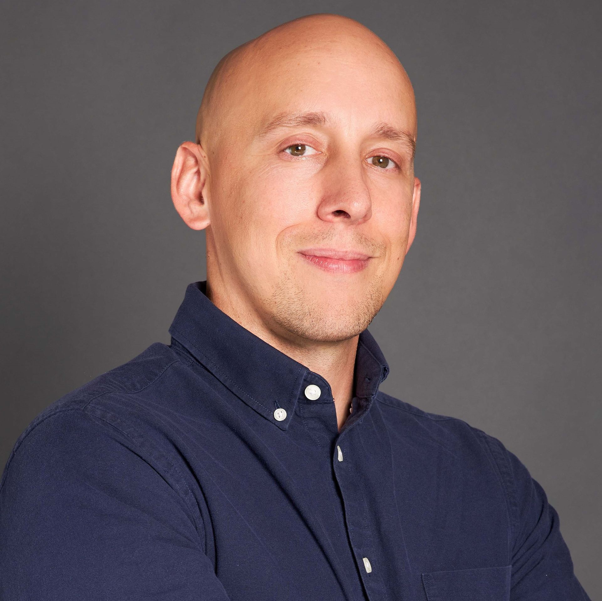 A bald man in a suit and tie is smiling for the camera.