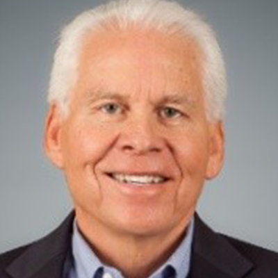 A man with white hair is wearing a suit and smiling.