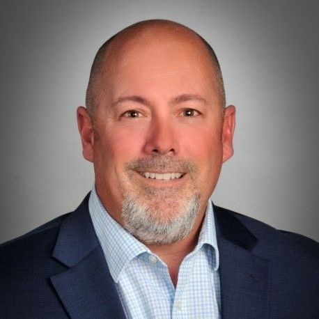 A bald man in a suit and tie is smiling for the camera.