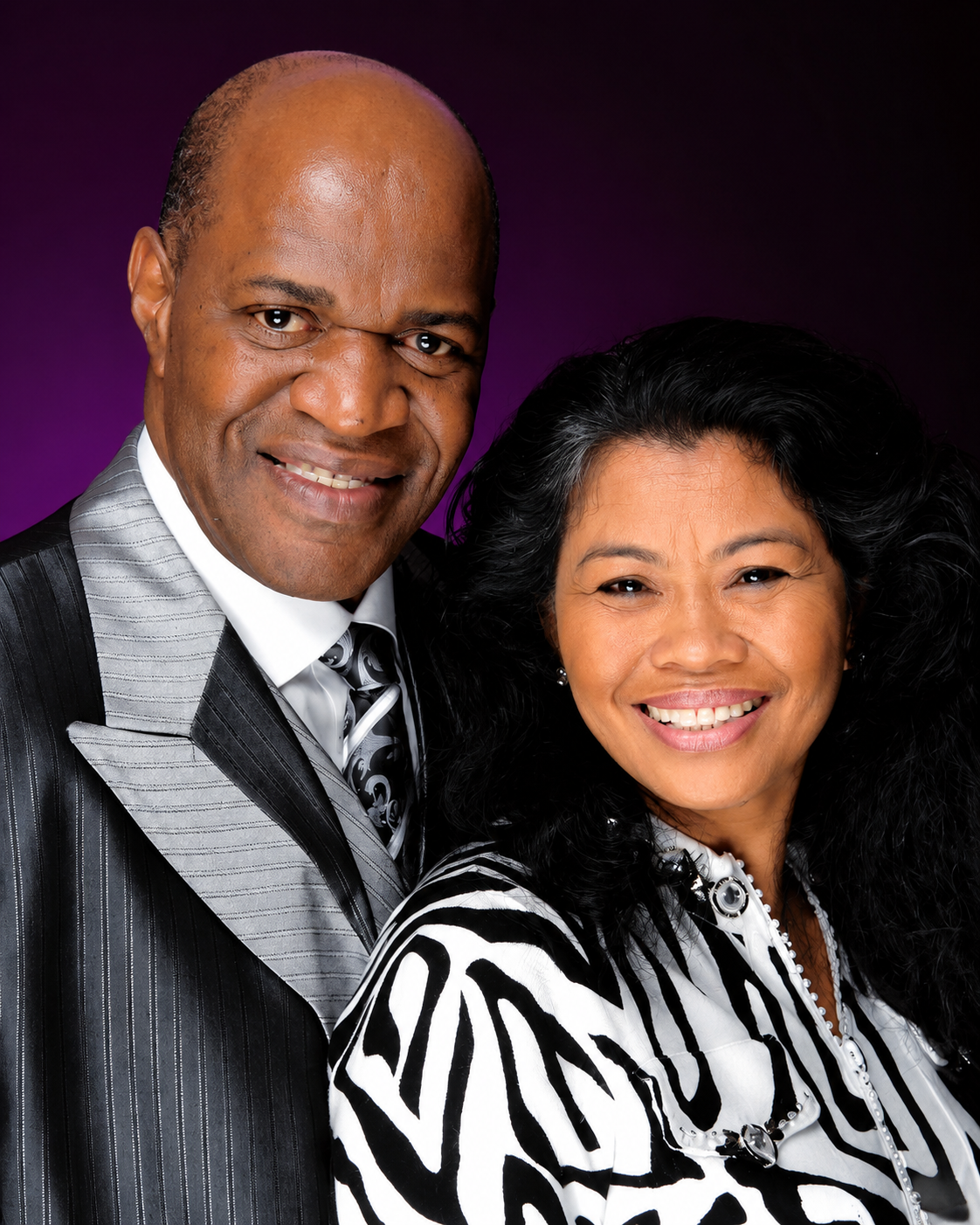 Smiling couple in formal attire posing against a dark purple studio backdrop