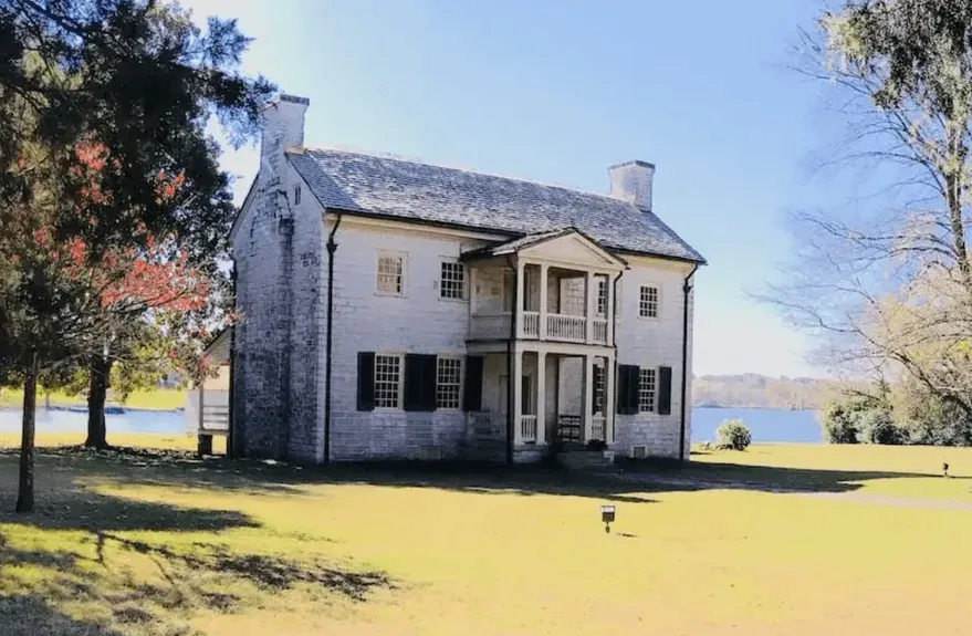 Two-story white brick house with a porch and water view, sunny day.