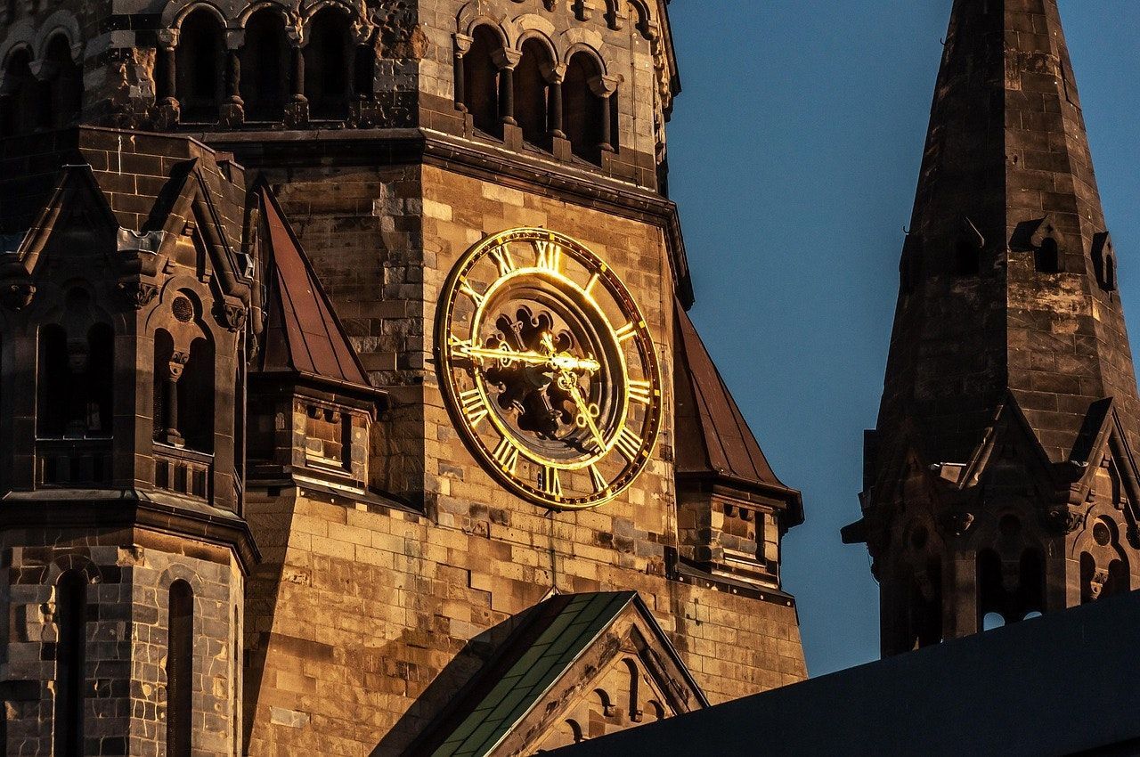 Clock tower with golden clock face against a blue sky, part of a tall church building.