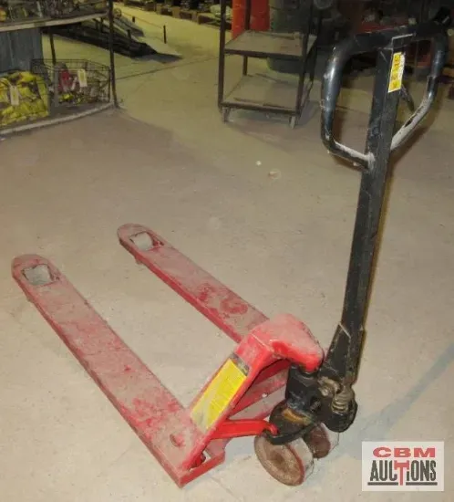 Red pallet jack on a concrete floor. Black handle. Dusty.
