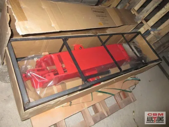 Red metal tractor attachment in a cardboard box with a black metal frame.