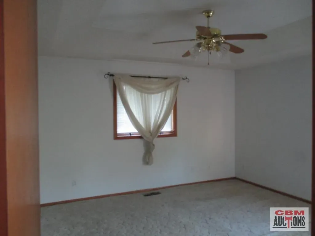 An empty room with a ceiling fan and a sign that says com auctions