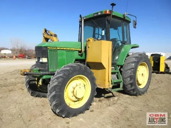 A green john deere tractor is parked in a dirt field