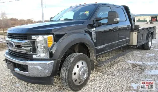 A black flatbed truck is parked on a gravel road.