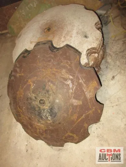 Two rusty, metal agricultural discs, one on top of the other, on a concrete surface.