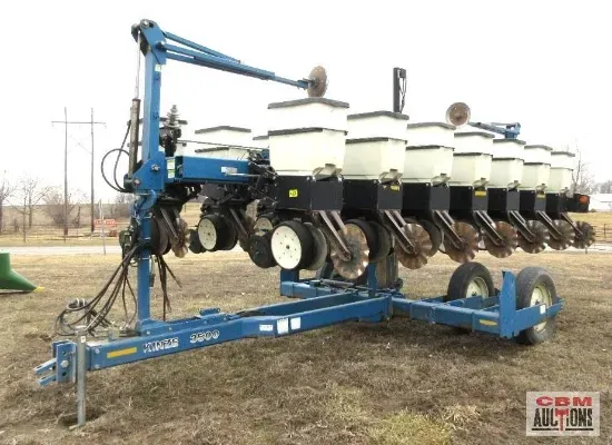 A row of planters are sitting on a trailer in a field.
