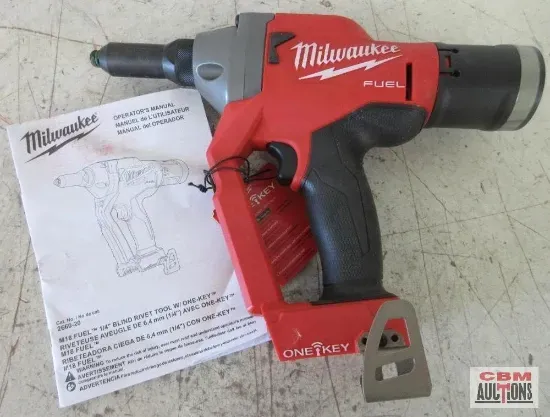 A lawn mower is parked in a gravel lot next to a wooden fence.
