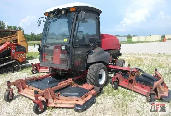 Red commercial riding mower with cabin and dual cutting decks on grass.