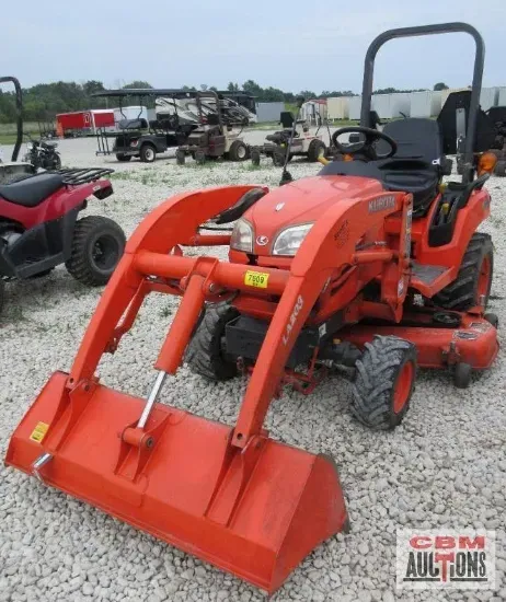 An orange tractor with a large orange bucket sits in a gravel lot