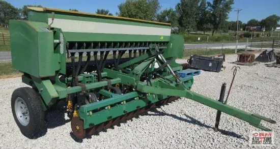 Green agricultural grain drill on a gravel lot.