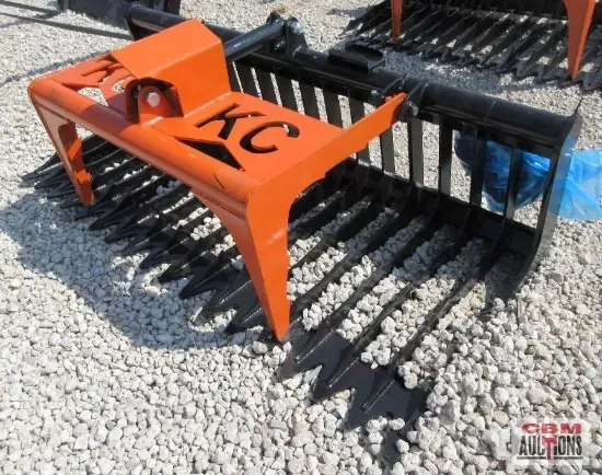 Orange and black rock grapple, possibly for a tractor, on a bed of gravel. 