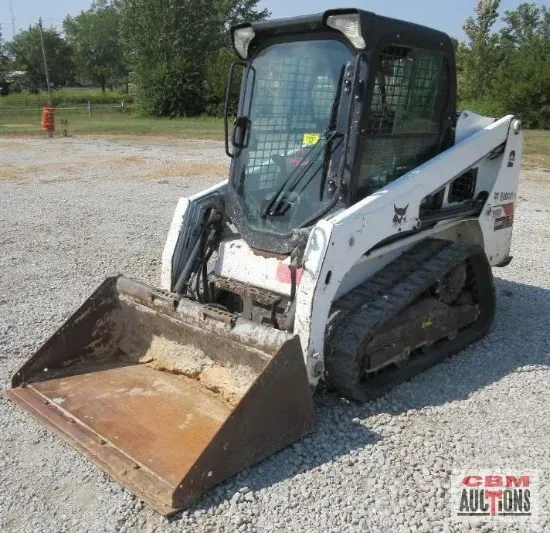 White Bobcat track loader with bucket in a gravel lot.